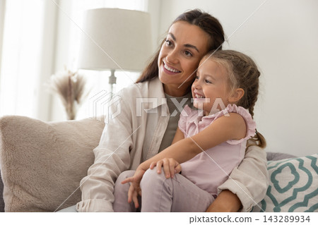 Affectionate mother relaxing on cozy sofa hugging little daughter dreaming 143289934