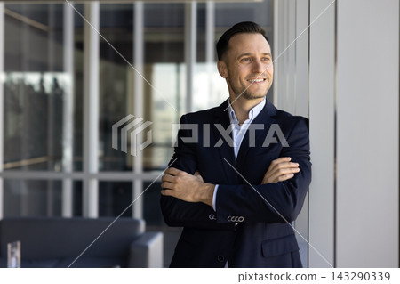 Confident businessman stands with folded arms, looks into distance thoughtfully Confident businessman stands with folded arms, looks into distance thoughtfully 143290339