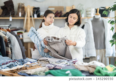 Adult woman and teenage girl choose jeans and trousers Adult woman and teenage girl choose jeans and trousers 143290550