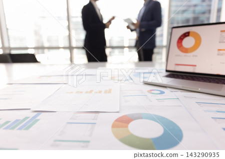 Closeup table with laptop and statistical documents with businesspeople communicating Closeup table with laptop and statistical documents with businesspeople communicating 143290935
