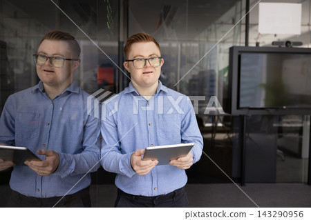 Young man with Down syndrome holding tablet in office Young man with Down syndrome holding tablet in office 143290956