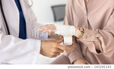 Traumatologist doctor wrapping bandage on woman patient arm in clinic Traumatologist doctor wrapping bandage on woman patient arm in clinic 143291143