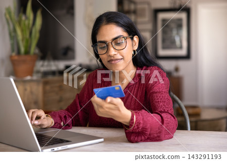 Woman sitting at table with laptop, holds card, shopping online Woman sitting at table with laptop, holds card, shopping online 143291193