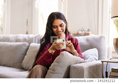 Young Indian woman sits on comfortable sofa at home Young Indian woman sits on comfortable sofa at home 143291212