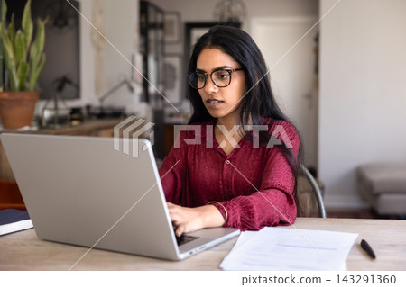 Young woman sits at table working on laptop at homeoffice Young woman sits at table working on laptop at homeoffice 143291360
