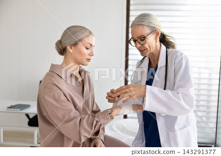 Female doctor wrapping bandage on patient arm in examination room 143291377