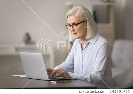Serious concentrated older age businesswoman type document on laptop 143291755