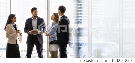 Businesspeople engaged in discussion standing near window in city office Businesspeople engaged in discussion standing near window in city office 143291839