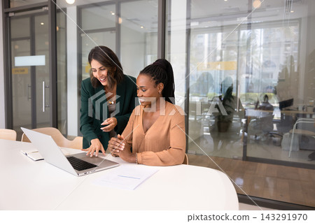 Smiling Hispanic woman explaining project details on laptop to colleague Smiling Hispanic woman explaining project details on laptop to colleague 143291970