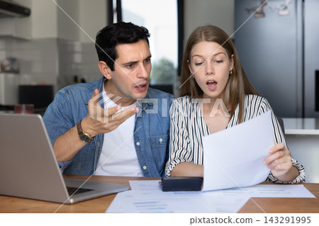 Shocked couple reviewing unexpected bills at home 143291995