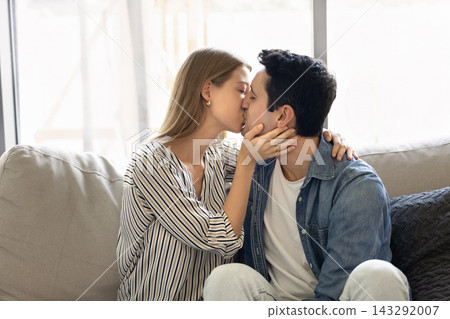 Young loving couple kissing sitting on cozy sofa Young loving couple kissing sitting on cozy sofa 143292007