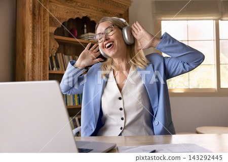 Caucasian businesswoman enjoying music with headphones at home office Caucasian businesswoman enjoying music with headphones at home office 143292445