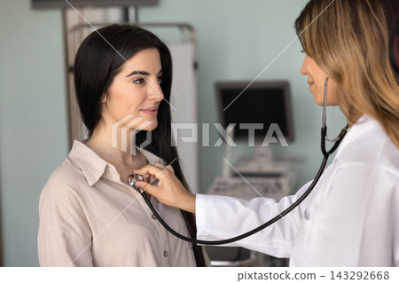 Female doctor listening to patient heartbeat with stethoscope 143292668