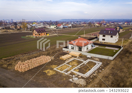 Aerial view of new house roof with attic windows and building site, foundation of future house, stacks of bricks and building timber logs for construction. Aerial view of new house roof with attic windows and building site, foundation of future house, stacks of bricks and building timber logs for construction. 143293022