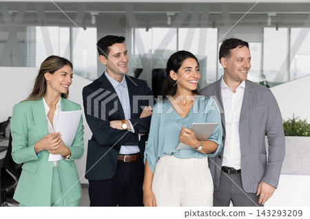 Diverse group of colleagues standing in office smiling looking aside Diverse group of colleagues standing in office smiling looking aside 143293209