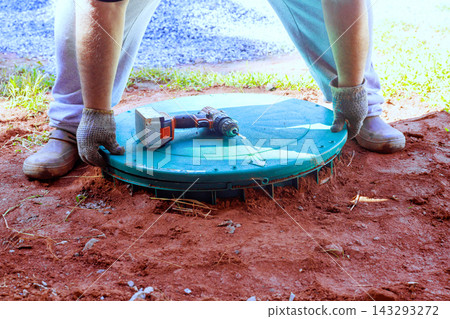 Worker places green cover over wastewater treatment tank in backyard Worker places green cover over wastewater treatment tank in backyard 143293272