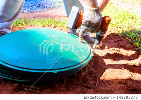 Builder is using drill to secure green cover on utility box in garden. 143293278