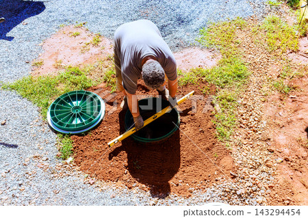 Carpenter is digging in ground of yard, checking an underground system in green container Carpenter is digging in ground of yard, checking an underground system in green container 143294454
