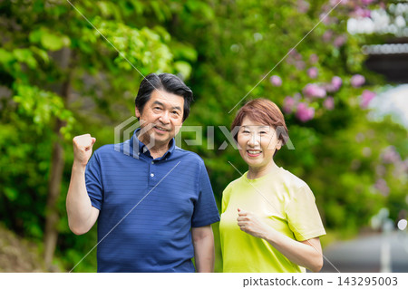 一對老年夫婦在綠樹環繞中面帶微笑,做出勝利的手勢。 一對老年夫婦在綠樹環繞中面帶微笑,做出勝利的手勢。 143295003