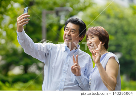 一對老年夫婦在綠地裡用智慧型手機拍照。 143295004