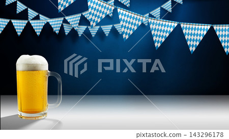 Mug of foamy beer on a white surface and blue-and-white checkered pennants hanging against a dark blue wall. Perfect for Bavarian festival promotions and party invitations. 143296178