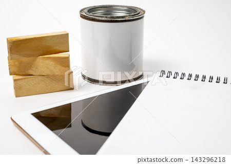 A close-up shot of an art and DIY creation setup featuring a blank paint can, three stacked wooden blocks, a spiral-bound notebook, and a white digital tablet against a clean white background. A close-up shot of an art and DIY creation setup featuring a blank paint can, three stacked wooden blocks, a spiral-bound notebook, and a white digital tablet against a clean white background. 143296218