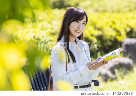 一位女士在陽光明媚的公園裡看書。 一位女士在陽光明媚的公園裡看書。 143297888