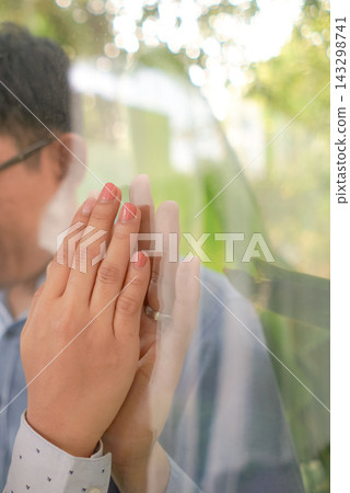 Two hands press against transparent glass surface in indoor space. Soft light and reflection create a quiet emotional mood. Two hands press against transparent glass surface in indoor space. Soft light and reflection create a quiet emotional mood. 143298741