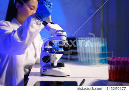 Female Scientist Using Microscope in Blue Lit Research Laboratory with Test Tubes and Samples Female Scientist Using Microscope in Blue Lit Research Laboratory with Test Tubes and Samples 143299677