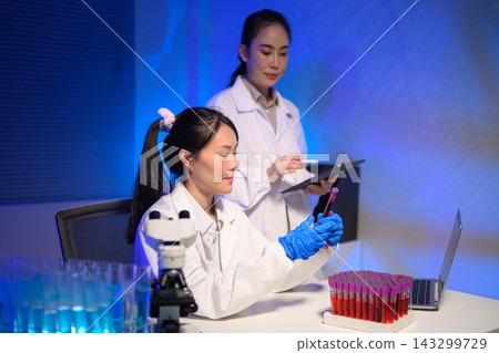 Two Female Scientists Working in Modern Laboratory with Blood Test Tubes and Microscope Two Female Scientists Working in Modern Laboratory with Blood Test Tubes and Microscope 143299729