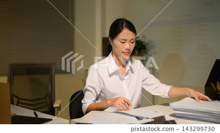 Stressed Businesswoman Working Late at Night Sorting Through Pile of Documents at Office Desk Stressed Businesswoman Working Late at Night Sorting Through Pile of Documents at Office Desk 143299730