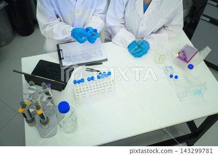 Two Scientists in White Lab Coats Collaborating at Laboratory Workbench with Test Tubes and Equipment Two Scientists in White Lab Coats Collaborating at Laboratory Workbench with Test Tubes and Equipment 143299781