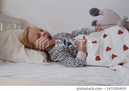 Angry little girl crying and throwing stuffed toy in bed 143300409