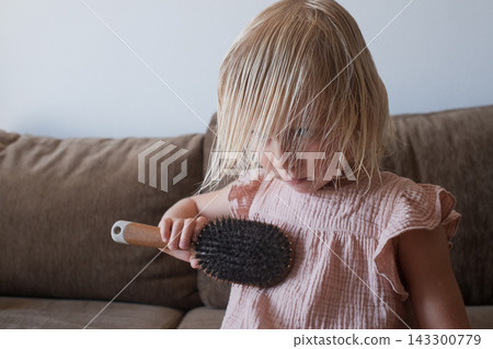 girl in a pink dress brushing her damp hair on a brown couch. 143300779