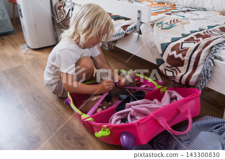 londe Toddler Girl Packing Toys and Clothes into a Bright Luggage in Her Bedroom londe Toddler Girl Packing Toys and Clothes into a Bright Luggage in Her Bedroom 143300830