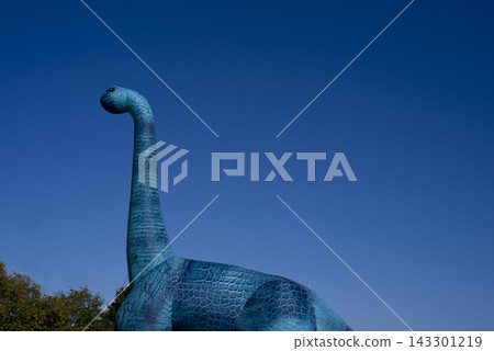 A landscape featuring dinosaurs. A blue dinosaur, created for an event, stands against a blue sky. 143301219