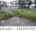 A small park in a residential area with overgrown grass. 143301359