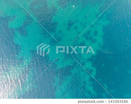 Clear Adriatic water off Budva, Montenegro displays turquoise shallows and darker submerged patches from above. Small pink float rests on rippled sea, while sunlight sparkles across open water. Clear Adriatic water off Budva, Montenegro displays turquoise shallows and darker submerged patches from above. Small pink float rests on rippled sea, while sunlight sparkles across open water. 143303580