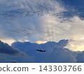 Silhouetted airplane flies through dramatic clouds with sunbeams piercing through the sky at twilight 143303766