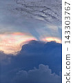 Vibrant rainbow halo forms above dark storm clouds with sunbeams piercing through twilight sky at high altitude 143303767