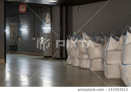 Industrial Warehouse Interior With Stacked Bulk Bags and White Sacks Stored on Concrete Floor Industrial Warehouse Interior With Stacked Bulk Bags and White Sacks Stored on Concrete Floor 143303813