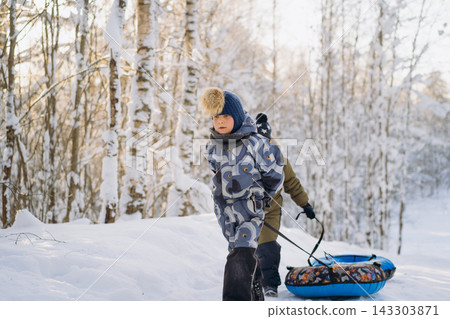 caucasian boys walking up the slope with snow tubing in forest on winter sunny day caucasian boys walking up the slope with snow tubing in forest on winter sunny day 143303871