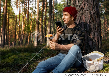 Man using smartphone app for mushroom identification in autumn forest. Scanning wild edible fungi with a smartphone camera checks safety, bolete species, and forest basket harvest. Man using smartphone app for mushroom identification in autumn forest. Scanning wild edible fungi with a smartphone camera checks safety, bolete species, and forest basket harvest. 143303897