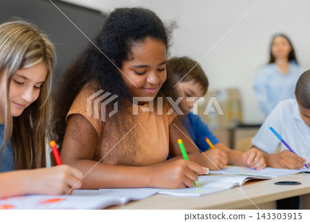 Diverse schoolchildren writing and drawing in notebooks together during classroom activity Diverse schoolchildren writing and drawing in notebooks together during classroom activity 143303915