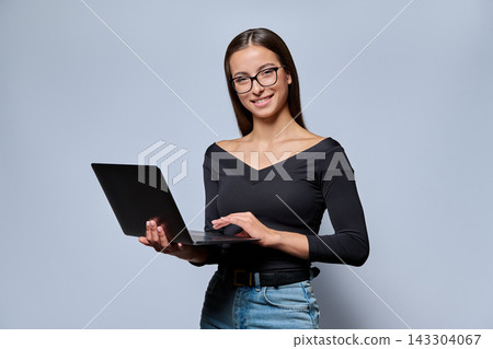 Young woman in glasses holding laptop and looking at camera in studio 143304067