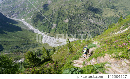 Hiker ascending steep rocky trail in Hohe Tauern National Park Austria with glacial valley and river below Hiker ascending steep rocky trail in Hohe Tauern National Park Austria with glacial valley and river below 143304227