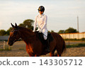Woman rider jockey in helmet and white uniform preparing horse racing. 143305712