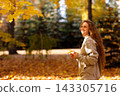 Smiling young woman walks in the autumn forest with the yellow leaves at sunset 143305716