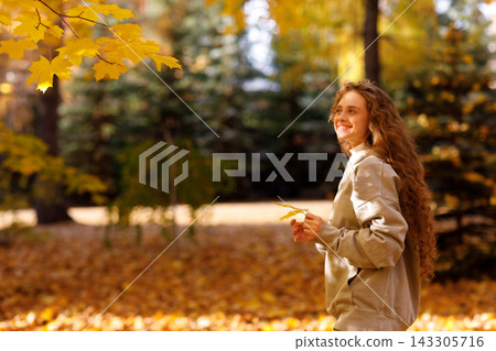 Smiling young woman walks in the autumn forest with the yellow leaves at sunset Smiling young woman walks in the autumn forest with the yellow leaves at sunset 143305716