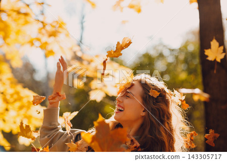 Smiling young woman throws up the autumn leaves in the forest at sunset. 143305717